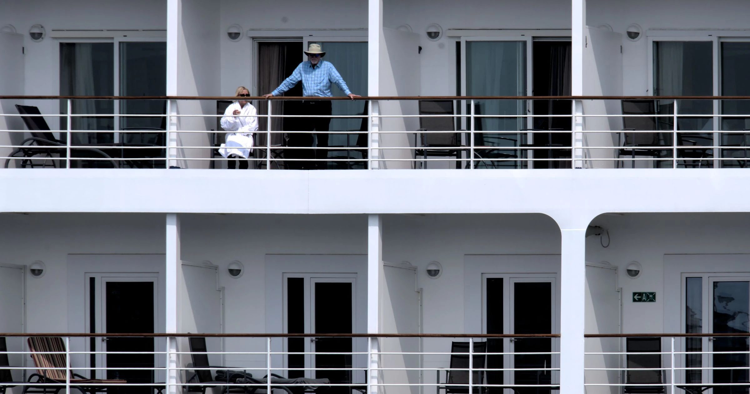 People relaxing on a cruise ship balcony, enjoying the ocean view and sunny weather.